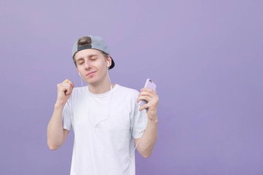 Sevimli genç adam bir beyaz T-shirt gözleri ile onun kulaklık müzik dinler bir pastel mor arka plan üzerinde kapalı. Müzik zevk. Mor arka planda müzik dans