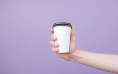 Kahve pastel mor arka plan üzerinde bir adamın elinde bardak.