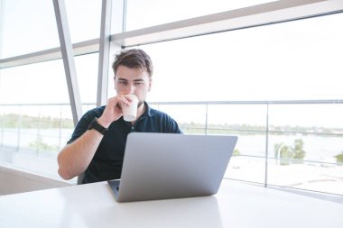 Çekici bir adam hafif bir kafede masada oturur, dizüstü bilgisayar ekranında görünüyor ve kahve içiyor. Sakallı işadamı pencerenin yakınındaki bir kafede bir dizüstü bilgisayar için çalışır.