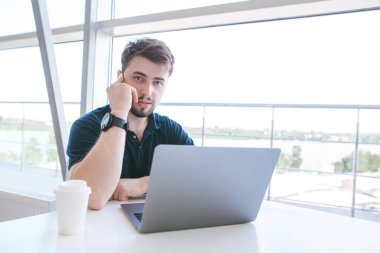 Çekici bir adam telefonda konuşurken ve kameraya bakarak bir defter ile bir fincan kahve, bir masada oturuyor. Bir kafede işyerinde meşgul iş adamı portresi.
