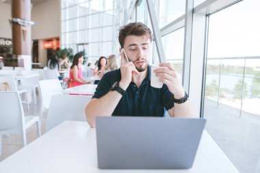 İş adamı elinde bir dizüstü bilgisayar ve bir bardak kahve ile bir kafede oturuyor, bir cep telefonu varmış. Kafede telefonla konuşmak. İş kavramı