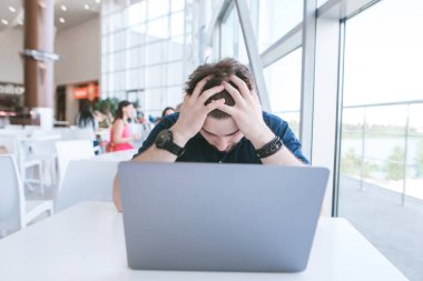 Bir kafede bir dizüstü bilgisayar üzerinde çalışan hayal kırıklığına uğramış bir adam portresi. Üzgün iş adamı başarısızlık başından düşürdü. İşadamı başarısız oldu.