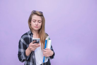 Ciddi kız casual giyim bir akıllı telefon kullanan ve defter ve Kitaplar mor arka planda tutar. Mor bir arka plan üzerinde izole bir akıllı telefon kullanan kadın. Boşaltmak