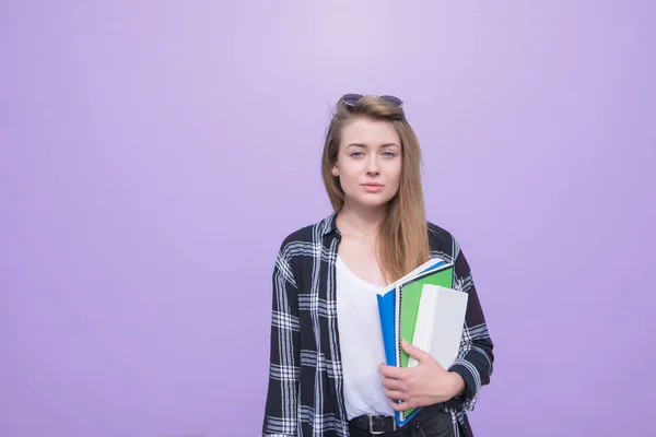 一个学生女孩的肖像站在紫色背景上 手里拿着书和笔记本 看着相机 严肃的学生是孤立的在紫色背景 — 图库照片