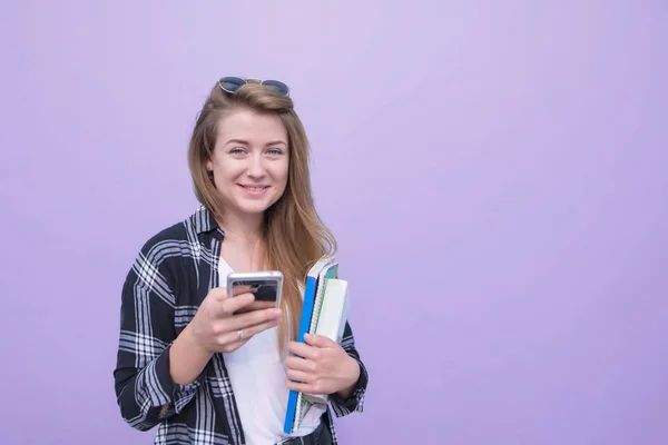有吸引力的学生女孩在紫色背景下被隔离 笔记本和智能手机在她的手看着相机和微笑 紫色背景下有雪球的女人 Copyspace — 图库照片