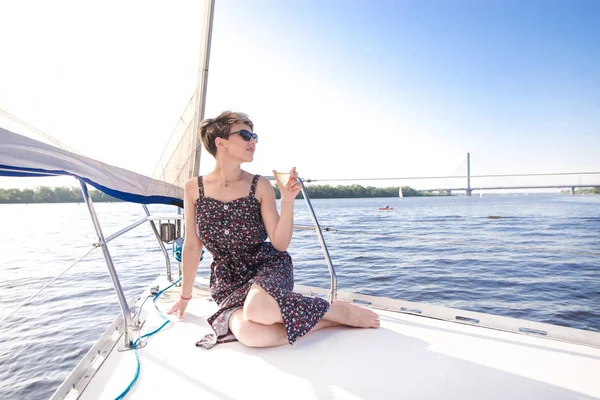 Attractive woman wearing glasses sits on the nose of a yacht with a glass of wine in her hands and floats along the sea. Beautiful woman resting on a yacht with a glass of wine.Swim in the yacht