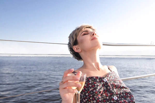 Attractive woman dressed in a dress is lying on a yacht against the sea with a glass of wine and relaxes.Closeup portrait of a woman on vacation, sailing on a yacht and drinking wine.Walk on the yacht