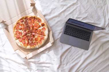 İştah açıcı pizza kutusu ve bir dizüstü bilgisayar yatak odasında katlanmış bir yatakta yalan söylüyorsun. Film ve pizza kutusu ile evde dinlenin. Boşaltmak
