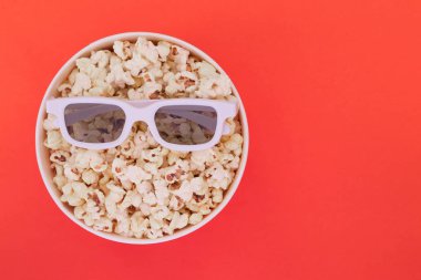 3D gözlük bir bardakta izole kırmızı bir arka plan üzerinde patlamış mısır ile yalan. Sinema kavramı. Düz yatıyordu. Boşaltmak.