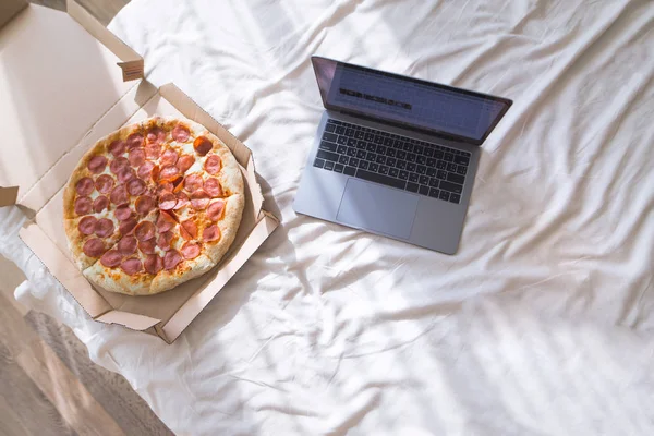 Laptop and box of pizza delivery are on the bed. Leisure at home with a laptop and pizza on a weekend.Copyspace