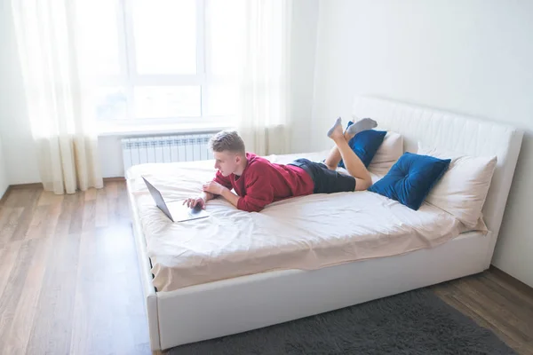 Молодой Человек Лежит Кровати Спальне Стильным Убогим Интерьером Работает Ноутбуке — стоковое фото