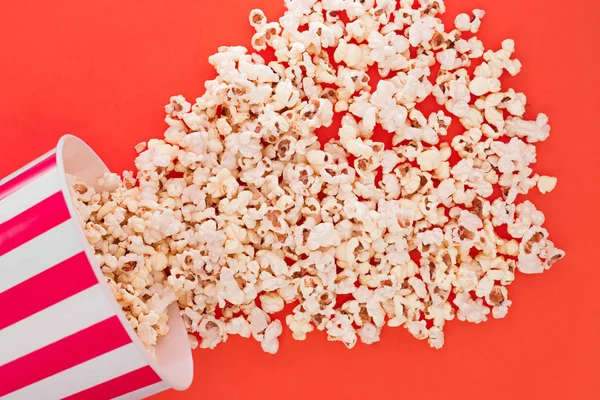 Popcorn rises from a paper bowl to a red background, a view from above. Cup with popcorn is isolated on a red background. Flat lay. Copyspace. Cinema Concept.