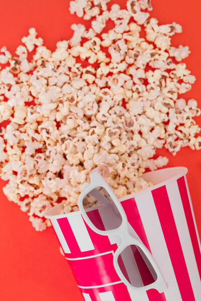 Popcorn in a paper bowl and 3d glasses for watching a film on a red background, top view. Flat lay. Copyspace. Cinema Concept.