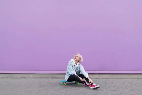 Menina Feliz Elegante Senta Skate Contra Uma Parede Roxa Sorri — Fotografia de Stock