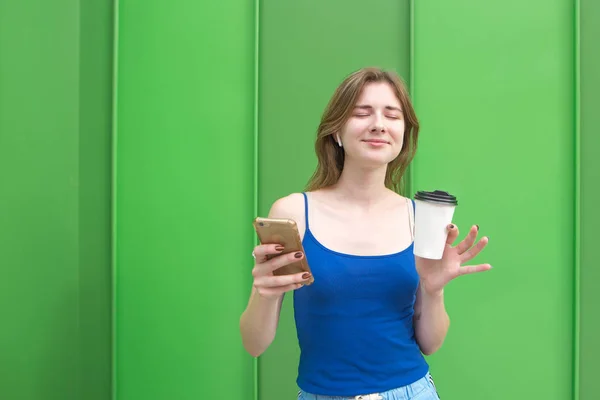Счастливая Женщина Стоит Фоне Зеленой Стены Смартфоном Стаканом Кофе Руках — стоковое фото