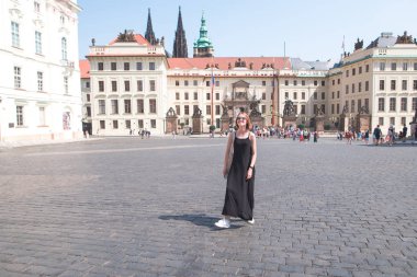 Mutlu bir siyah elbise kız pozlar Prag sokaklarında bir güneşli yaz gününde. Çekici, şık kız gülümser ve eski şehrin sokaklarında yürüyüş.