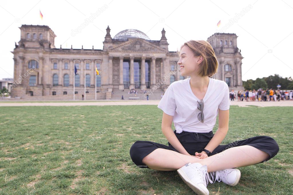 Portrait of a happy young girl sitting on the background of a historic building and smiling. Happy girl traveler in Berlin, Germany on the background of the Reichstag.