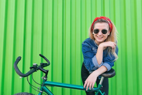 緑の壁の背景に自転車でスタイリッシュな服ポーズで幸せな女は カメラと笑顔を見てください 緑の壁の背景に自転車で笑顔の女子生徒 — ストック写真