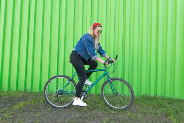 Girl Wearing Denim Jacket Glasses Rides Bike Background Green Wall — Stock Photo, Image