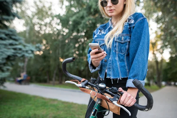 时髦的女孩停在自行车和使用智能手机 体育和技术 自行车的妇女使用互联网在智能手机在公园 — 图库照片