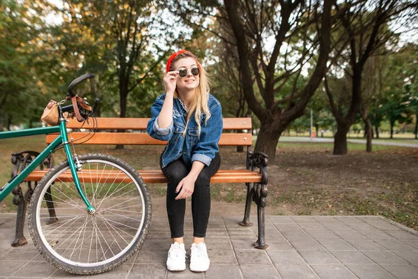 微笑时尚的女孩坐在公园的长凳上 自行车和休息 在公园休息 — 图库照片
