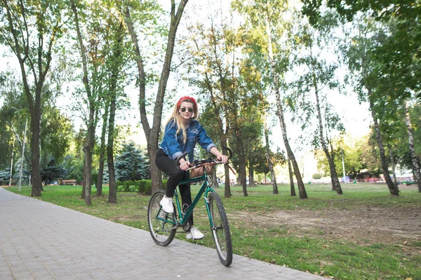 穿着时髦衣服和太阳镜的年轻女孩在公园里骑着绿色的自行车 在自行车上走 活动休闲理念 — 图库照片