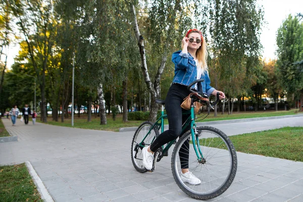 穿着太阳镜的时尚美女坐在公园的自行车上 时髦的女孩在公园里骑自行车 活动休息 — 图库照片