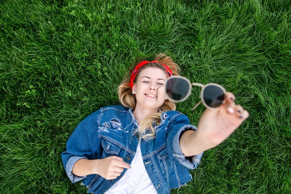 Happy Girl Denim Jacket Lying Green Lawn Holding Sunglasses Her — Stock Photo, Image