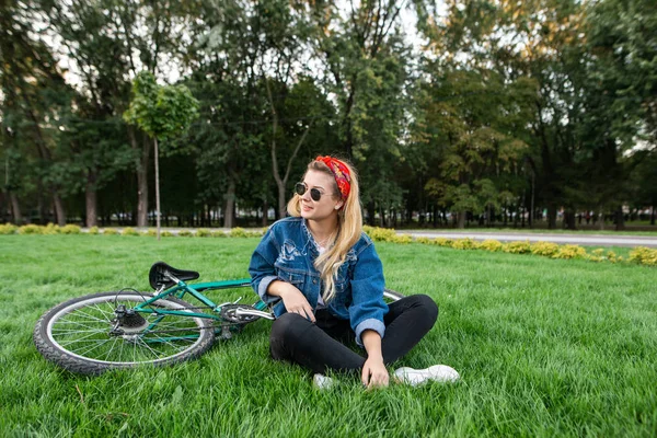 时尚迷人的年轻女子坐在草坪上的草坪上的草地上 微笑着 漂亮的女孩穿着时髦的衣服 在骑自行车的时候躺在草地上 户外放松 — 图库照片