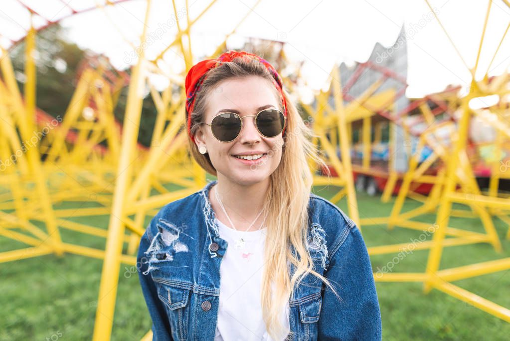 Portrait of a happy girl in stylish clothes standing on the background of a yellow slide in the park and smiles.