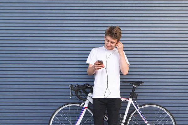 긍정적인 젊은이 자전거 스탠드 헤드폰에서 음악을 Smartphone에 보인다 배경에 자전거와 — 스톡 사진