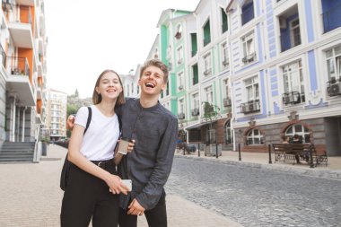 Güzel genç bir çift bir kucaklama şehirde dolaşan ve gülümseyen turist. Şehrin arka planı mutlu bir genç çift portresi. Açık sevgi dolu çift konuşmak ve gülümseyen