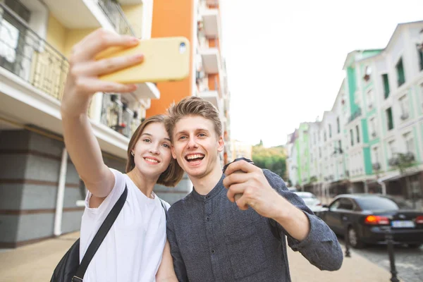 快乐的微笑年轻夫妇摆在相机和采取自拍智能手机 她带着自拍在镇上街上的一个年轻人那里 一起快乐 自拍理念 — 图库照片