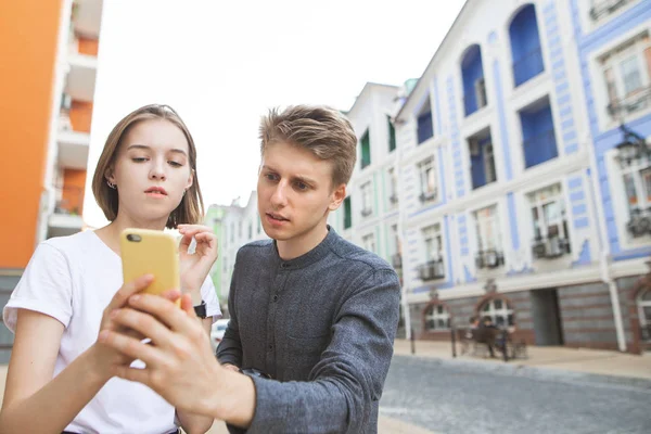 美丽的年轻夫妇在城市漫步时使用智能手机 年轻人和一个女孩正在看着智能手机的屏幕 街道肖像 在地图上搜索路线 — 图库照片