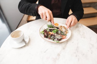 İş adam yeme salata Restoran yakın çekim. Eller bir adam ile bir bıçak bir çatalı salata, bir fincan kahve bir masada yemek. Sağlıklı beslenme.