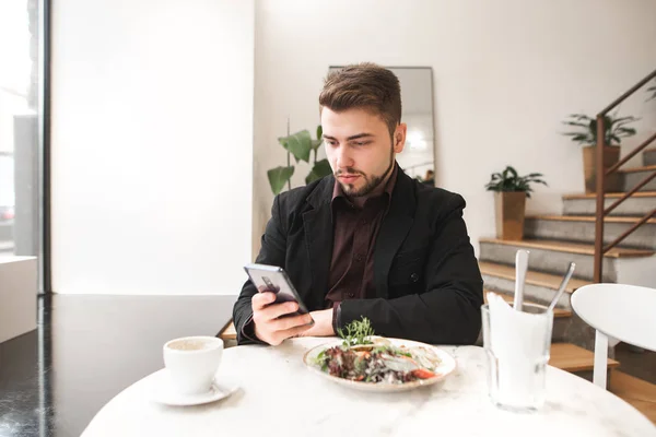 Business man with a beard sitting in a cozy restaurant at the table, eating salad and looking at the camera. Portrait of a businessman at breakfast in the bright caf.