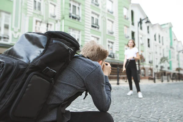 グレーのシャツとバックパックでプロの写真家は 町の路上で女の子を撮影しました カメラマンに焦点を当てます プロのカメラマンは Photosession — ストック写真