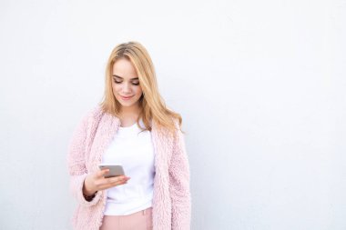 Güzel kız pembe ceket ve beyaz T-shirt bir smartphone ve gülümsüyor üzerinde beyaz bir arka plan kullanır. Aattractive Bayan smartphone üzerinde bir ileti yazar. Boşaltmak