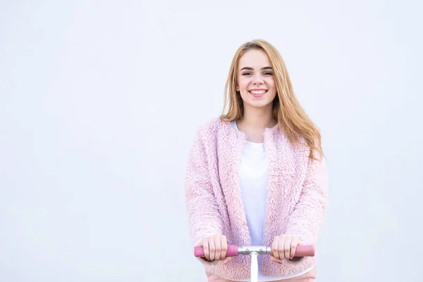 时尚的女孩与踢摩托车粉红色的衣服站在白色的背景 看着镜头和微笑 向左的复制空间 — 图库照片