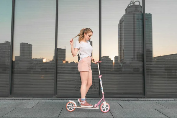 尾と暗いミラー壁の背景にピンクのスクーターに立っている白いシャツで魅力的な女の子 Copyspace スクーターの上を歩く — ストック写真