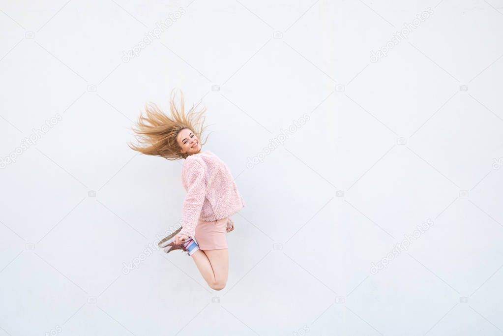 Happy girl in a pink dress in a jump on the background of a white wall smiles. Levitation concept. Copyspace