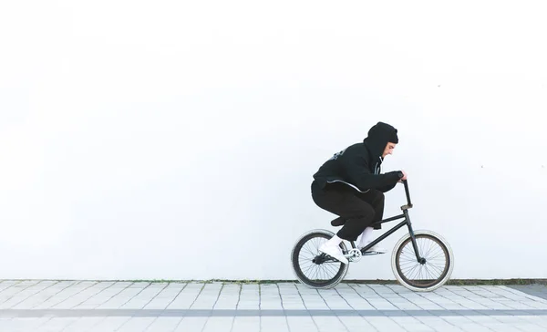 Bmx rider in casual clothing rides a bicycle on the background of a white wall. Bmx concept. Street freestyle on bmx