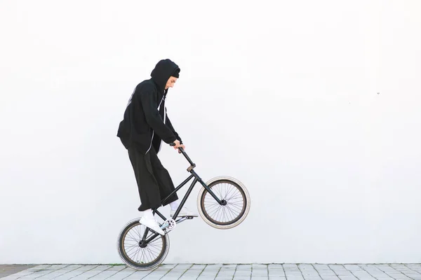 Bmx racer makes a trick in against the background of a white wall. Bmx rider with a bicycle in flight on a white background. Street bmx freestyle