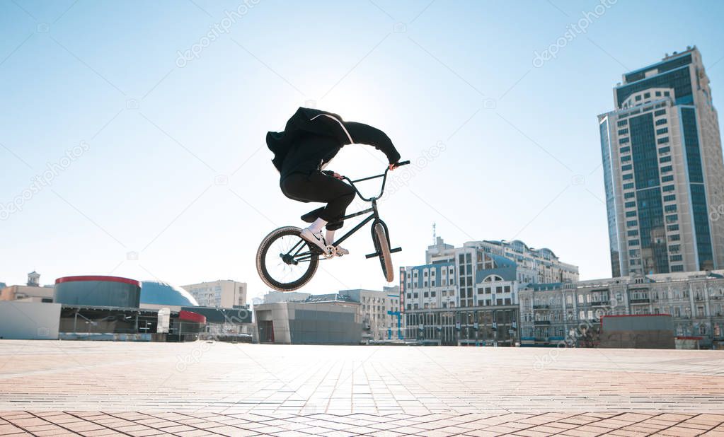 Silhouette of a bmx rider jumping against the backdrop of the sun and urban landscape on a bright summer day. Bmx cyclist makes complex tricks on a bike