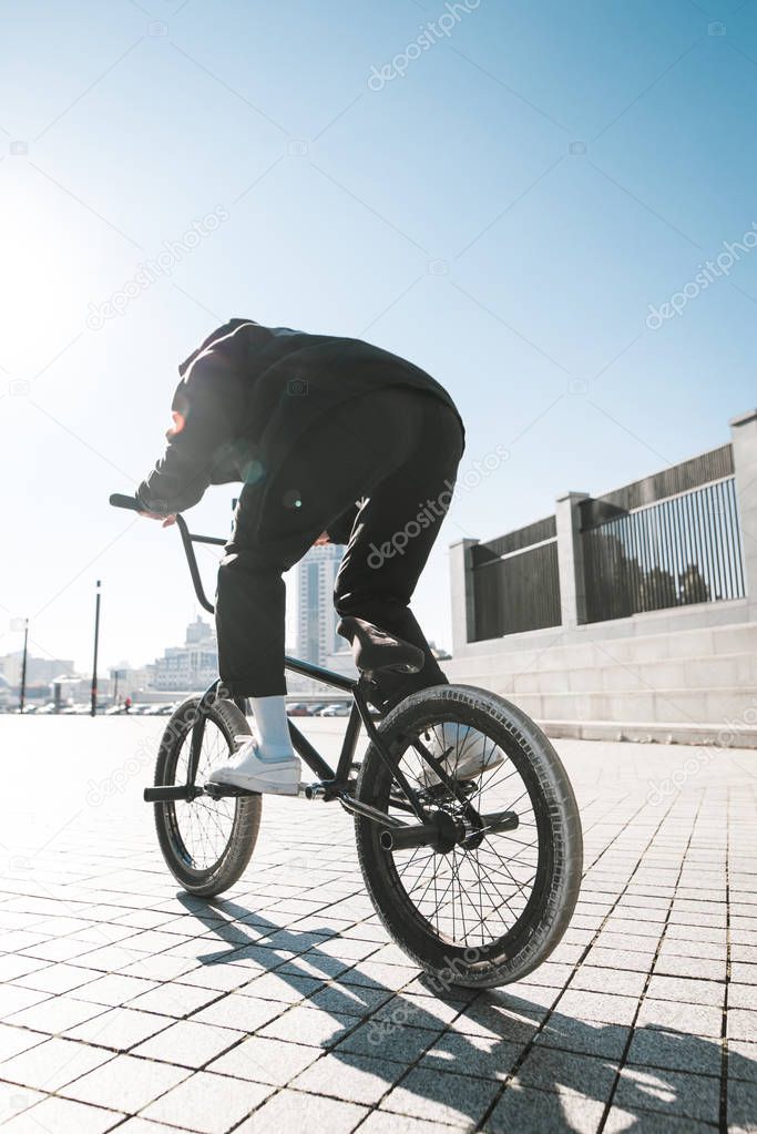 Young man in casual clothing rides a bmx on a sunny summer day. Bmx rider's back. Bmx concept