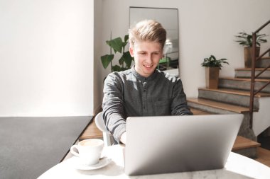 Gülümseyen ve ekrana bakarak bir dizüstü bilgisayar ile bir kafede oturan mutlu bir genç adam. Öğrenci bir kafede bir dizüstü bilgisayarda çalışır. Bir kafede çalışmak