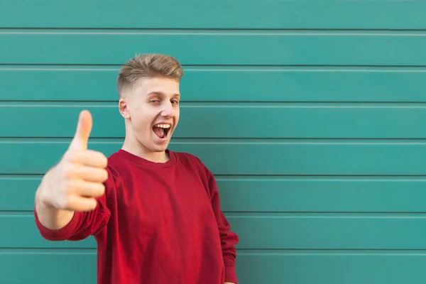 Впечатляющий Молодой Человек Стоит Фоне Бирюзовой Стены Показывая Большие Пальцы — стоковое фото