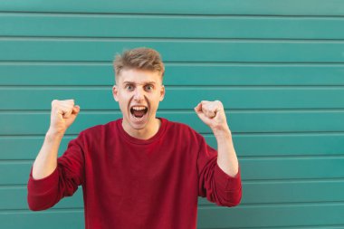 Çılgın neşeli genç adam elleriyle kaldırdı, sevinir turkuaz arka plan ve kutsal metin yer. Genç adam kazandı. Boşaltmak