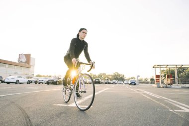 Genç adam koyu spor giyim ve bir kap beyaz bisiklet güneş park yerinde giyer. Bir bisikletçi öğrenci portresi. Bisiklete binme hobi.