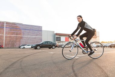 Sevimli genç bir adam bir park yeri modern mimari bir arka plan üzerinde sürme portresi. Park yerinde bisiklet binici.